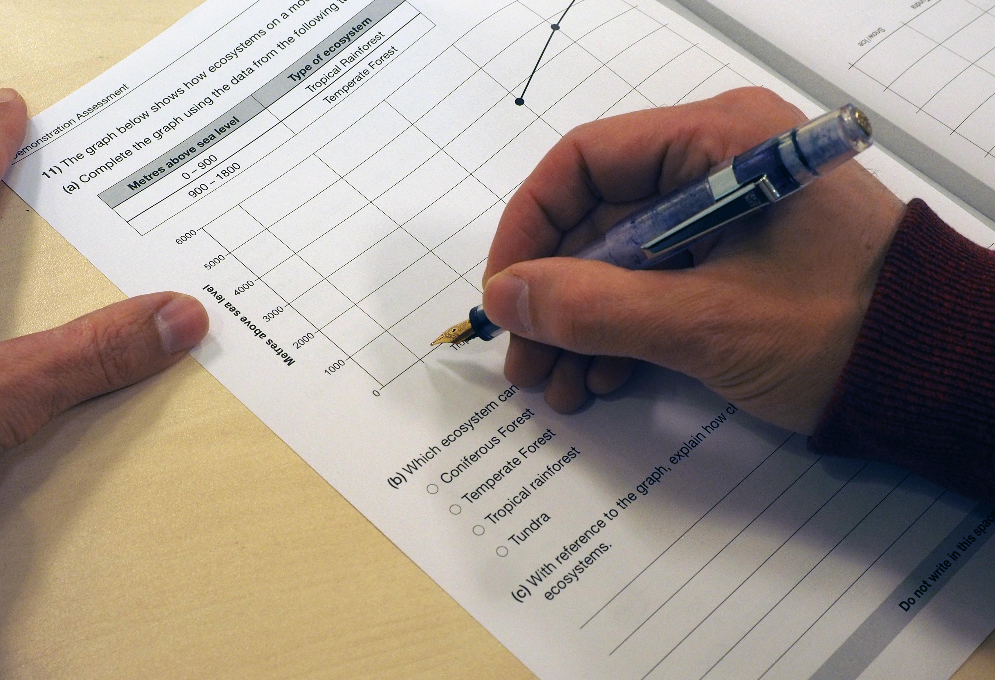 Learner using a pen to answer questions on a paper assessment