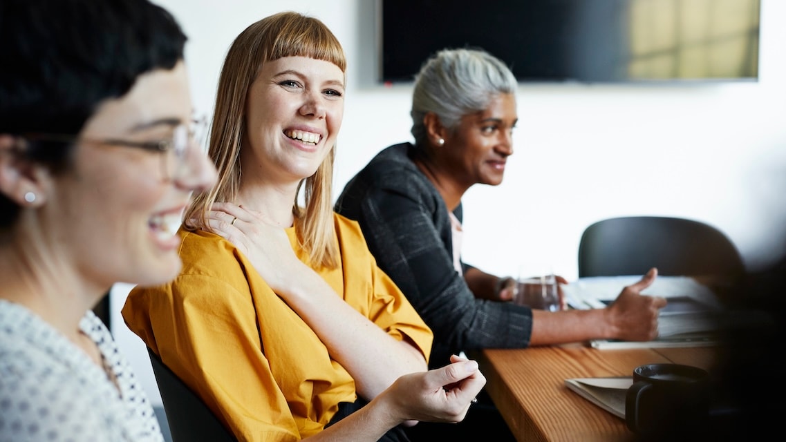 Colleagues seated around a meeting table in a bright office, engaged in discussion while reviewing notes and materials during a team session.