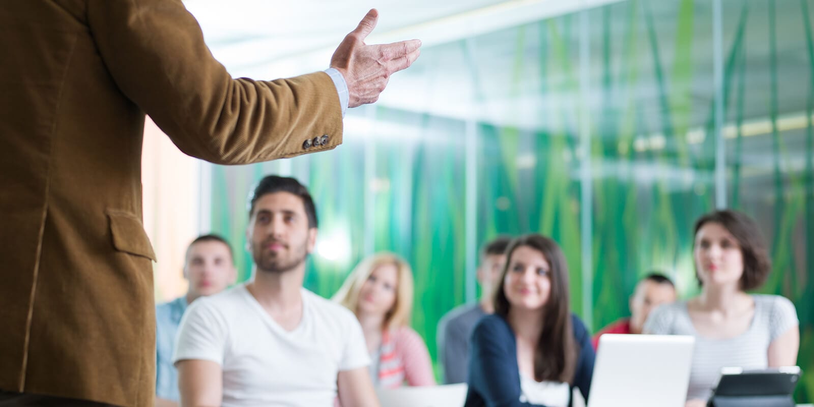A teacher pictured from the back gestures at attentive students