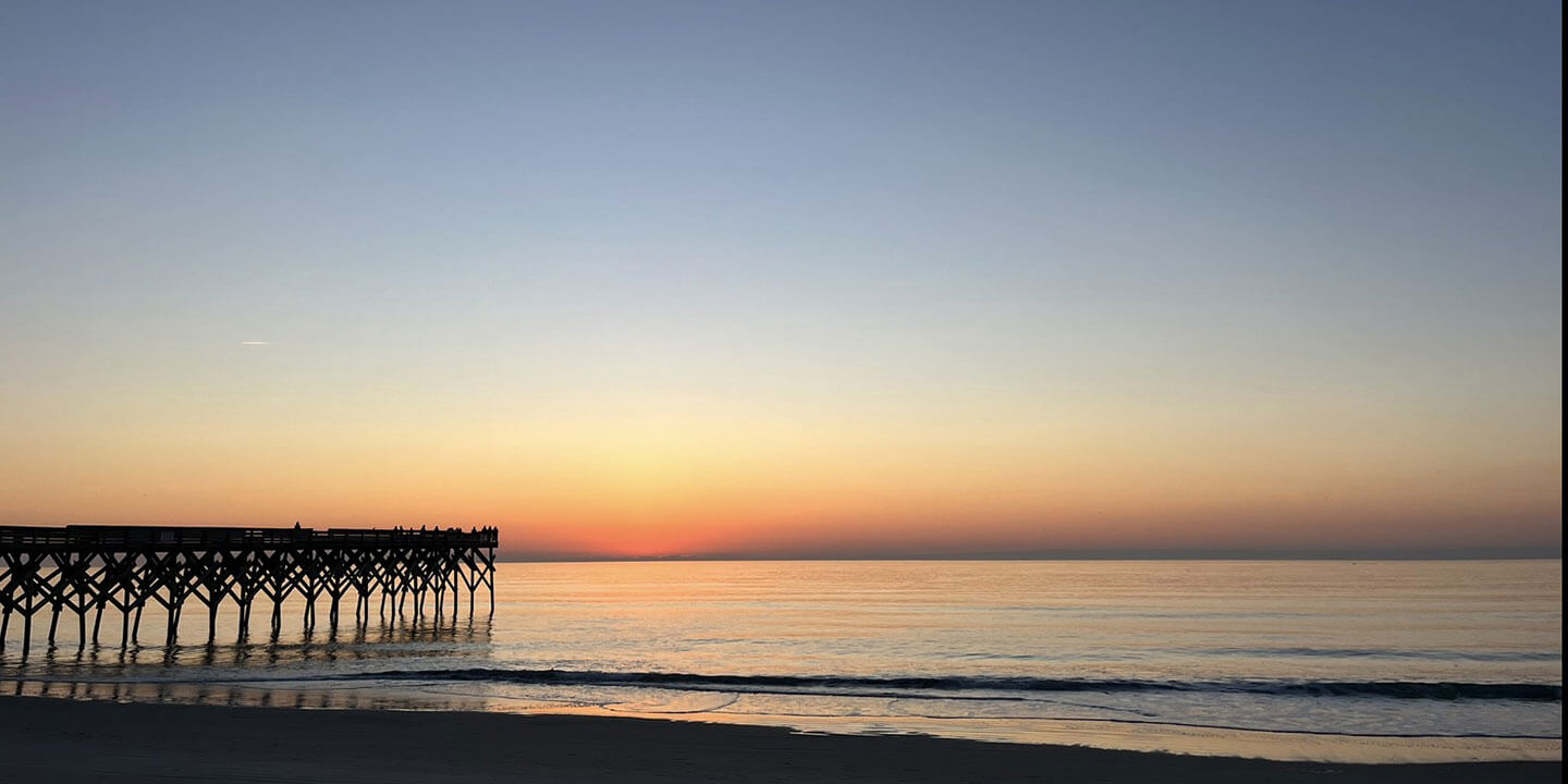 A view of a body of water at sunrise. There is a silhouetted dock on the left side.