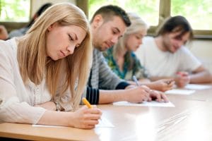 Higher education students sit at a desk and take a pen and paper test. 