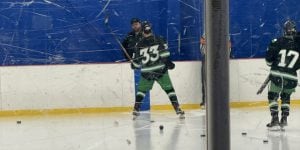 A collegiate hockey player on the ice at the University of North Texas. He is wearing green hockey pants and a black jersey with the number 33.