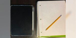 A tablet with a smart pen next to a spiral notebook opened to a blank page with a pencil on top.