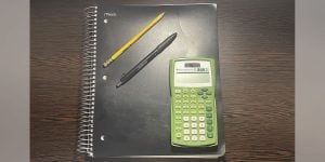 A composition notebook set on a desk with a pencil, pen, and green calculator.