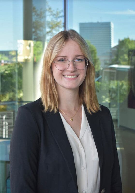 Blog author Cassandra is standing in front of a large office window. She has medium length blonde hair and is wearing glasses and a navy blazer over a white blouse.