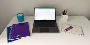 A white desk with 2 spiral notebooks, an open laptop, and a pencil holder.