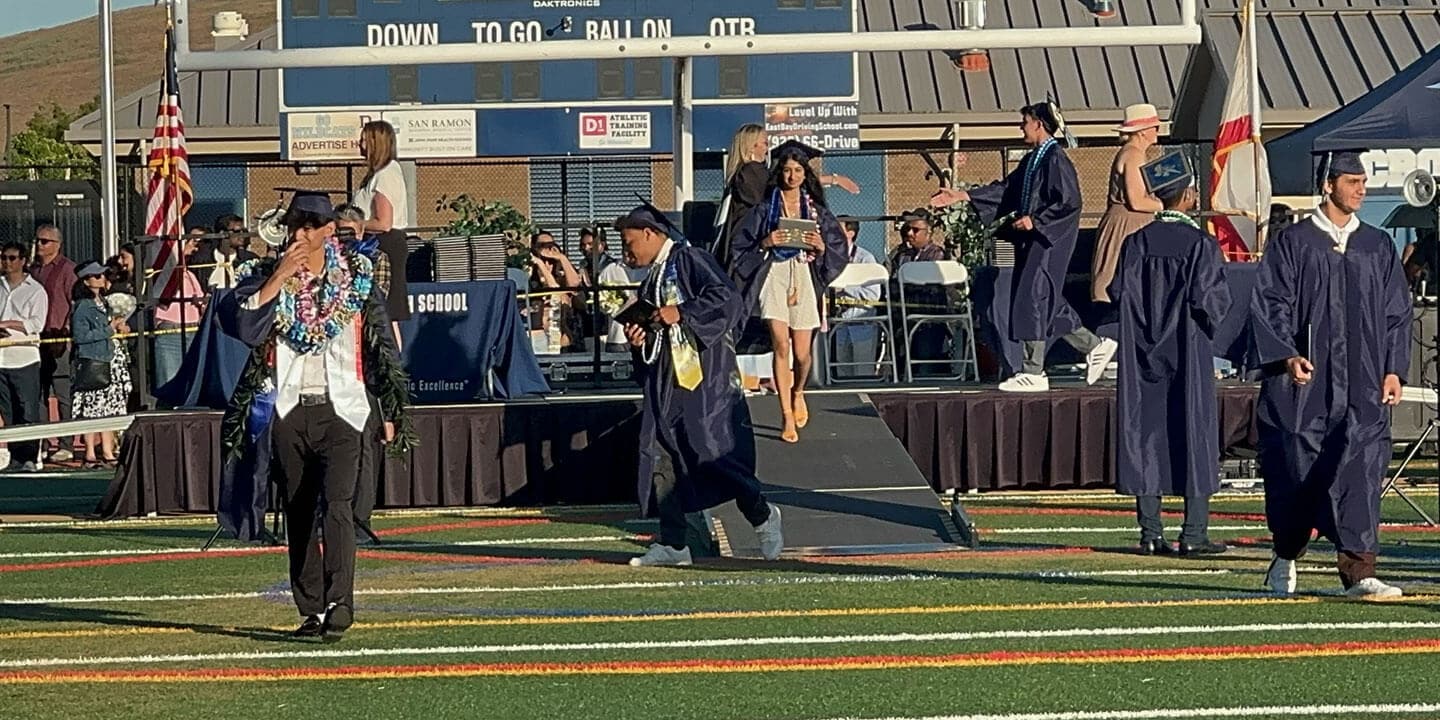 A young woman wearing a blue cap and gown. exits the stage after receiving her diploma. 