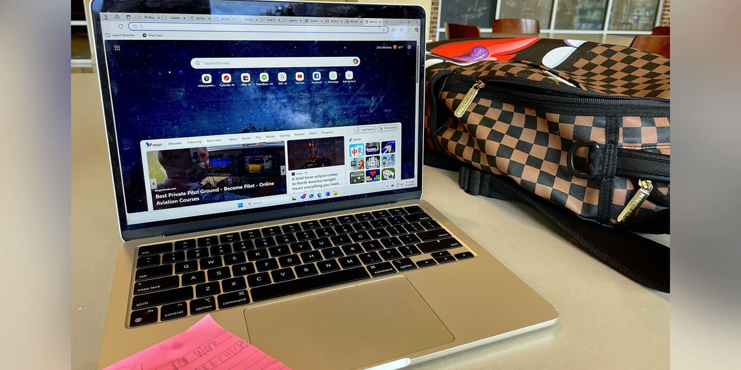 A student’s open laptop on a desk next to a brown and black checkered backpack.