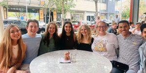 A group of 8 college students sitting around a table on an outdoor patio.
