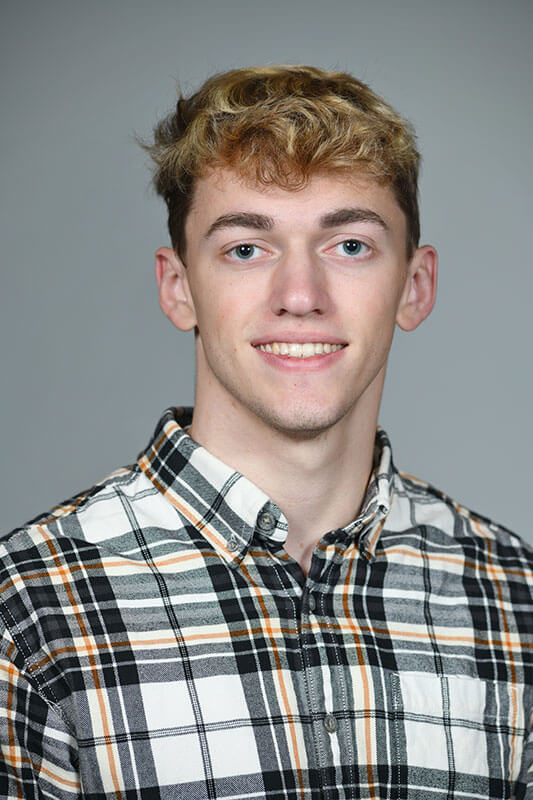 Blog author Jackson has short curly blonde hair and is wearing a white, black, and orange plaid shirt.