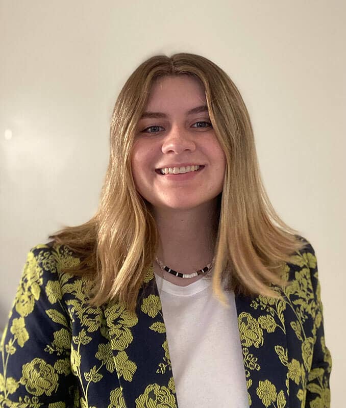 Blog author Jordan has long blonde hair and is wearing a navy blazer with yellow flowers over a light blouse.