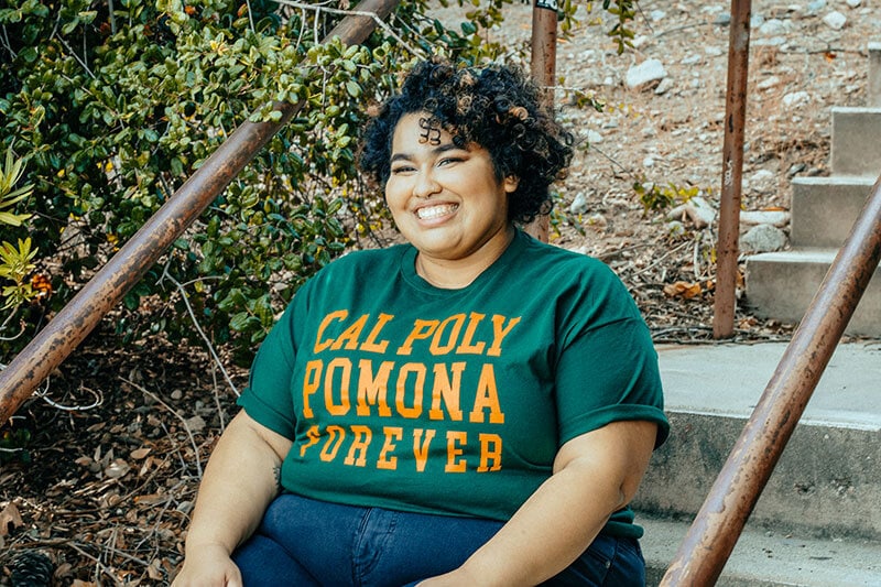 Blog author Katie is sitting on concrete steps and wearing a green Cal Poly Pomona t-shirt.