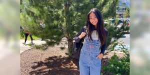 Blog author Kiahna is outside in front of a big tree. She is wearing overalls and has a backpack slung over one shoulder.