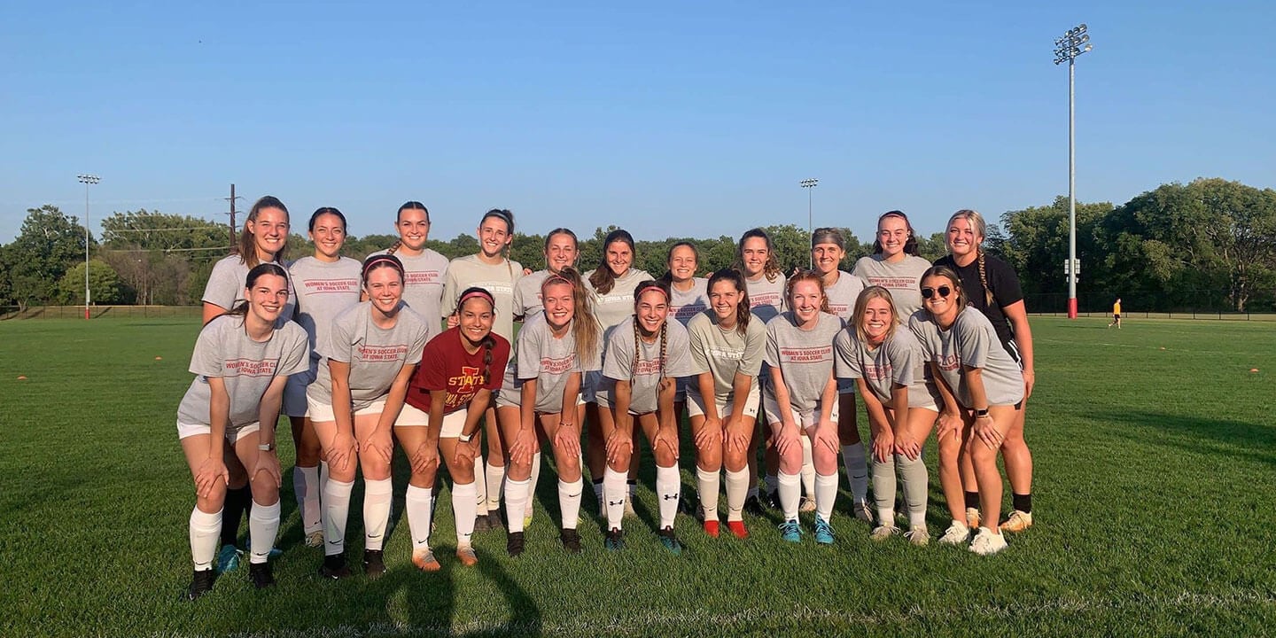 The Iowa State women’s club soccer team stands together outside on a soccer field.
