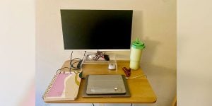 A student’s desk with a closed laptop, planner, and external monitor surrounded by various items such as a water bottle and hair clip.