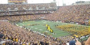 A full football stadium at the University of Iowa. The marching band is on the field and many fans are wearing black and gold.