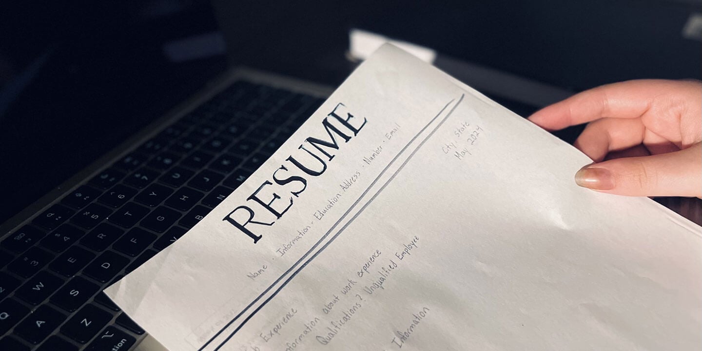 A close up of someone’s hand holding a written draft of a resume.