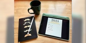 A notebook, coffee mug, and iPad with a list of 2024 resolutions arranged on a table. 