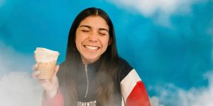 Blog author Mia is standing against a blue sky with white cloud background, holding a coffee-to-go cup. She has her eyes closed and is smiling.