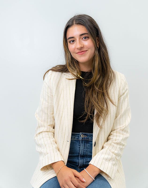Blog author Molly is sitting with her hands in her lap. She has long straight brown hair and is wearing a cream-colored blazer over a dark shirt and jeans.