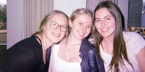 Three college women leaning in towards each other and smiling at the camera.