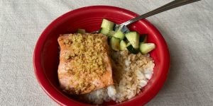 A red bowl on a table filled with a healthy meal of rice, salmon, and chopped zucchini.