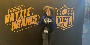Blog author Nia is standing in front of a large backdrop with the logos of HBCU Battle of the Brains and the NFL. 