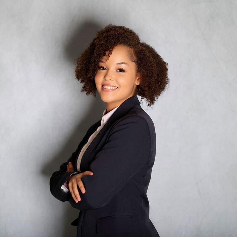 Blog author Nia has short curly hair and is standing sideways with her arms crossed. She is wearing a dark blazer over a light-colored blouse.