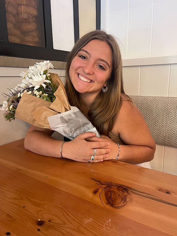Blog author Peyton is sitting at a restaurant booth holding a bouquet of flowers.