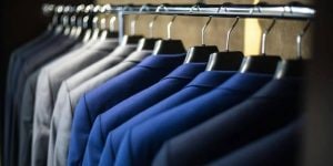 A clothes rack with a row of black, blue, tan, and grey blazers hanging from silver hangers.