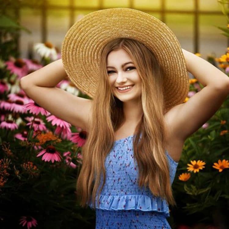 Blog author Taylor Perline is smiling. She has long blonde hair with a straw, wide brimmed hat on. She is wearing a blue dress. 
