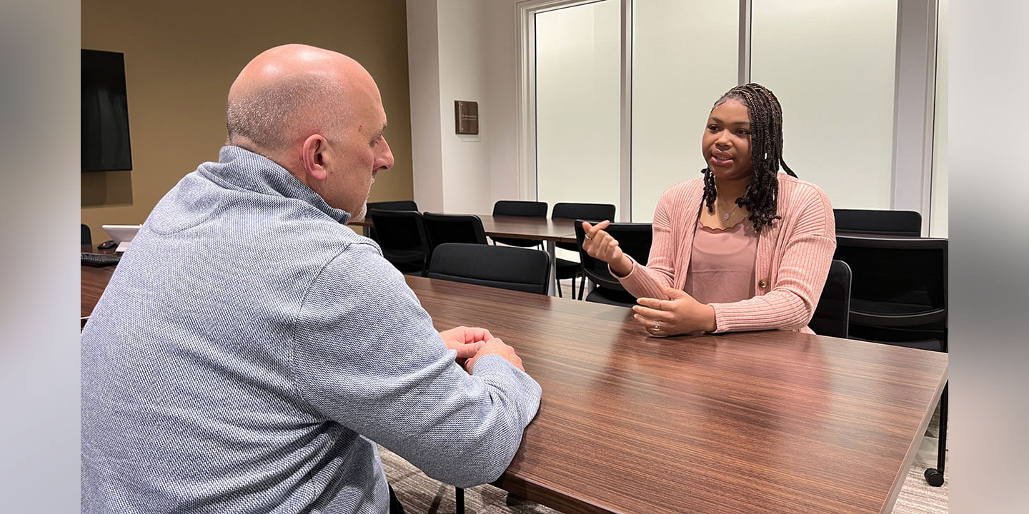 A man and a young college woman sitting at a table for an interview.