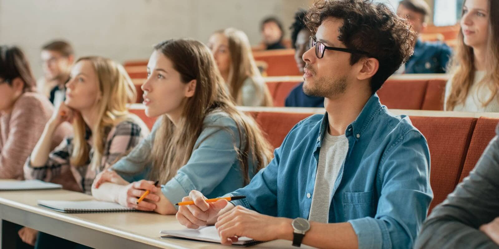Closeup of a row of students, listening to a ninstructor, while writing down information
