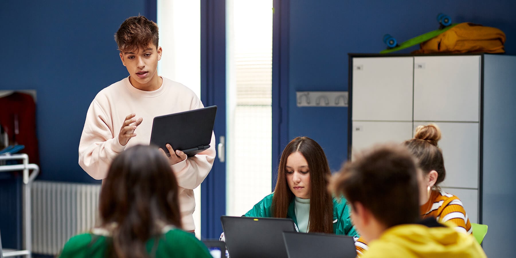 A group of high school-aged  students in a well lit room, interacting with each other.