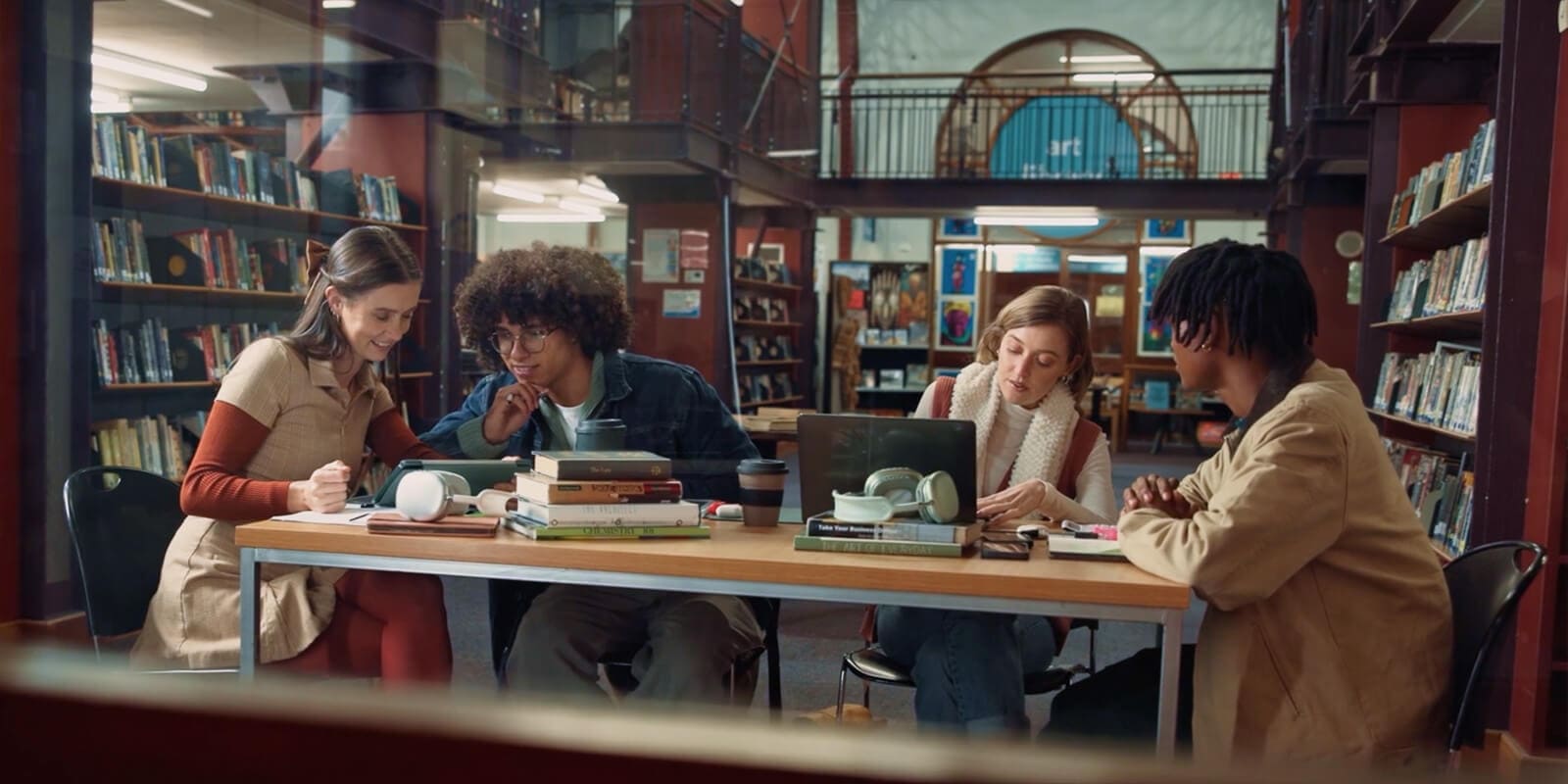 Students sitting around a table in a library with books and digital devices