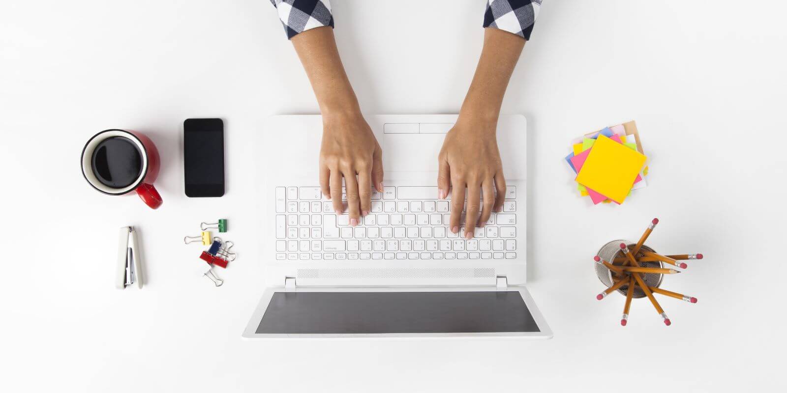 Image from above a desk, viewing a laptop, mobile device, coffee cup, pencils