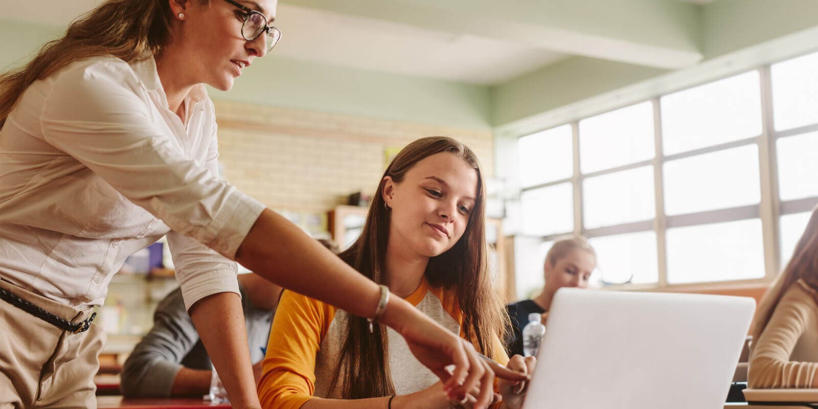 Female instructor in a classroom pointing out something on the laptop of a female student