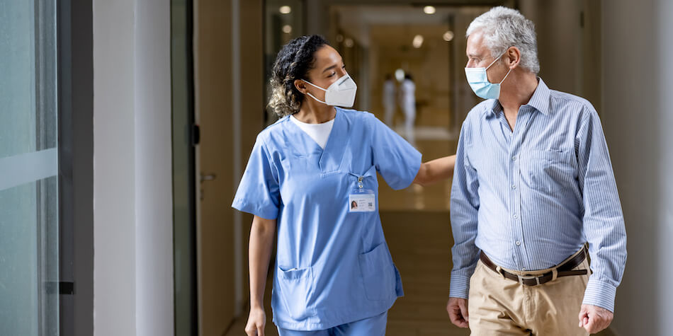 Image of health care professional and patient walking in a hallway, with protective masks on their faces