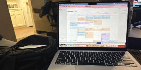 The picture shows a laptop showing an Outlook calendar filled with multicolored appointments.