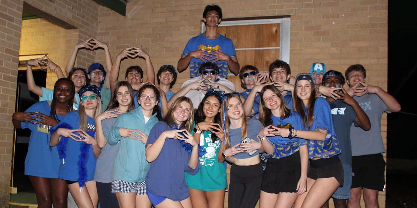 A group of students smiling and posing with interlocking fingers.