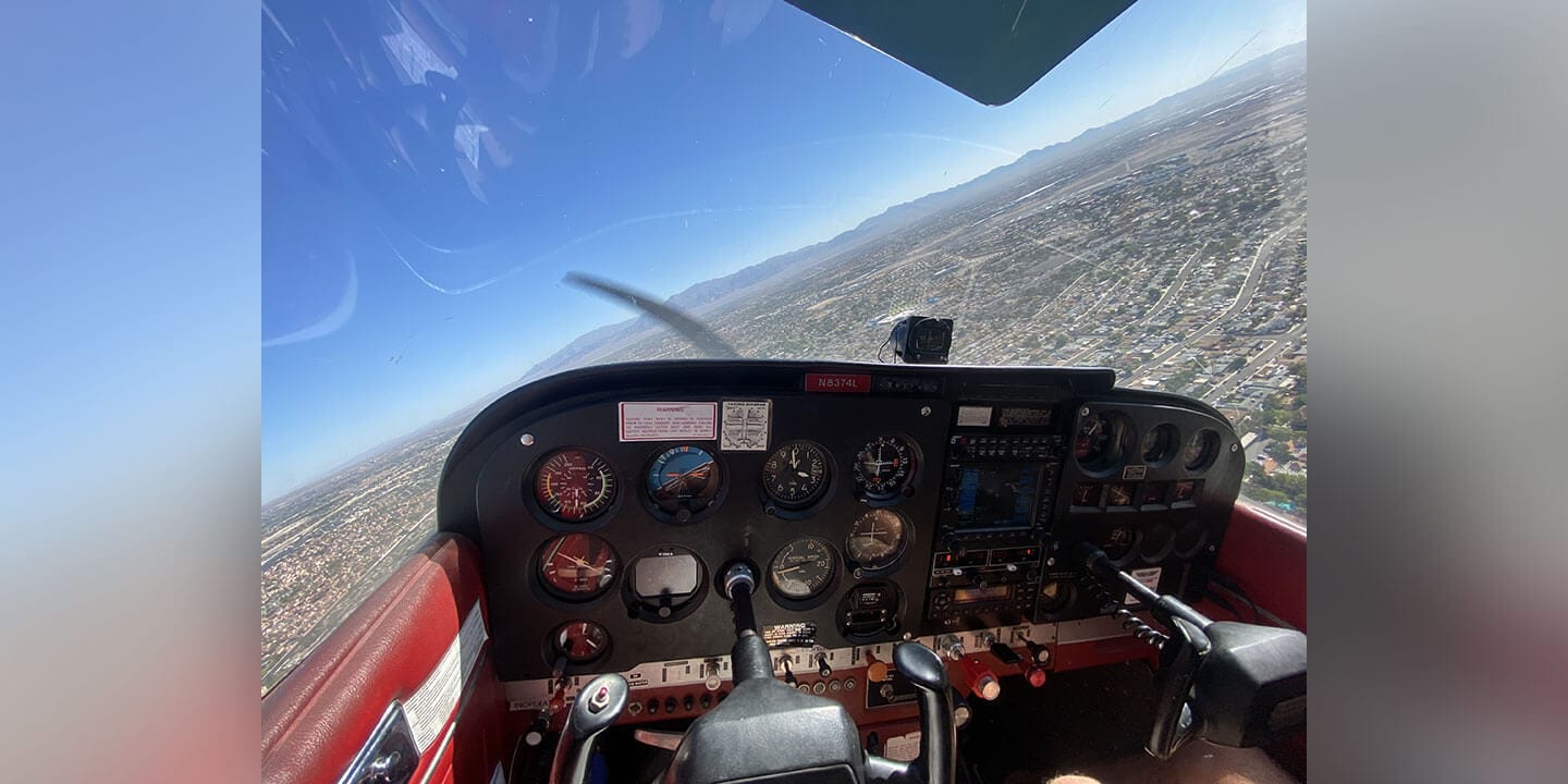 Image shows a view from a small plane's cockpit on a clear day with blue skies.