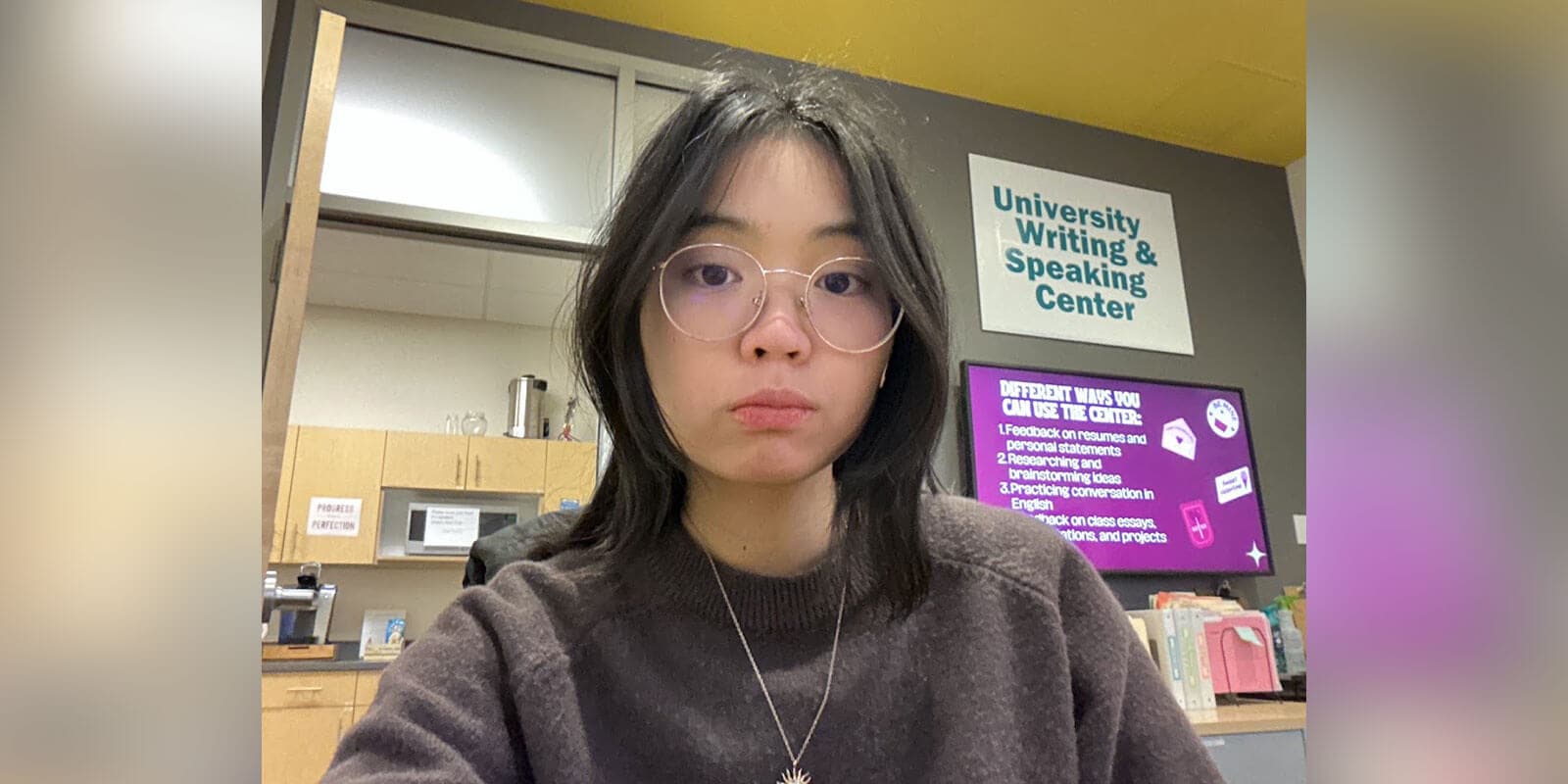 The photo shows a student inside a University Writing & Speaking Center. A display behind them promotes support for résumés, personal statements, research, brainstorming, and English conversation practice.
