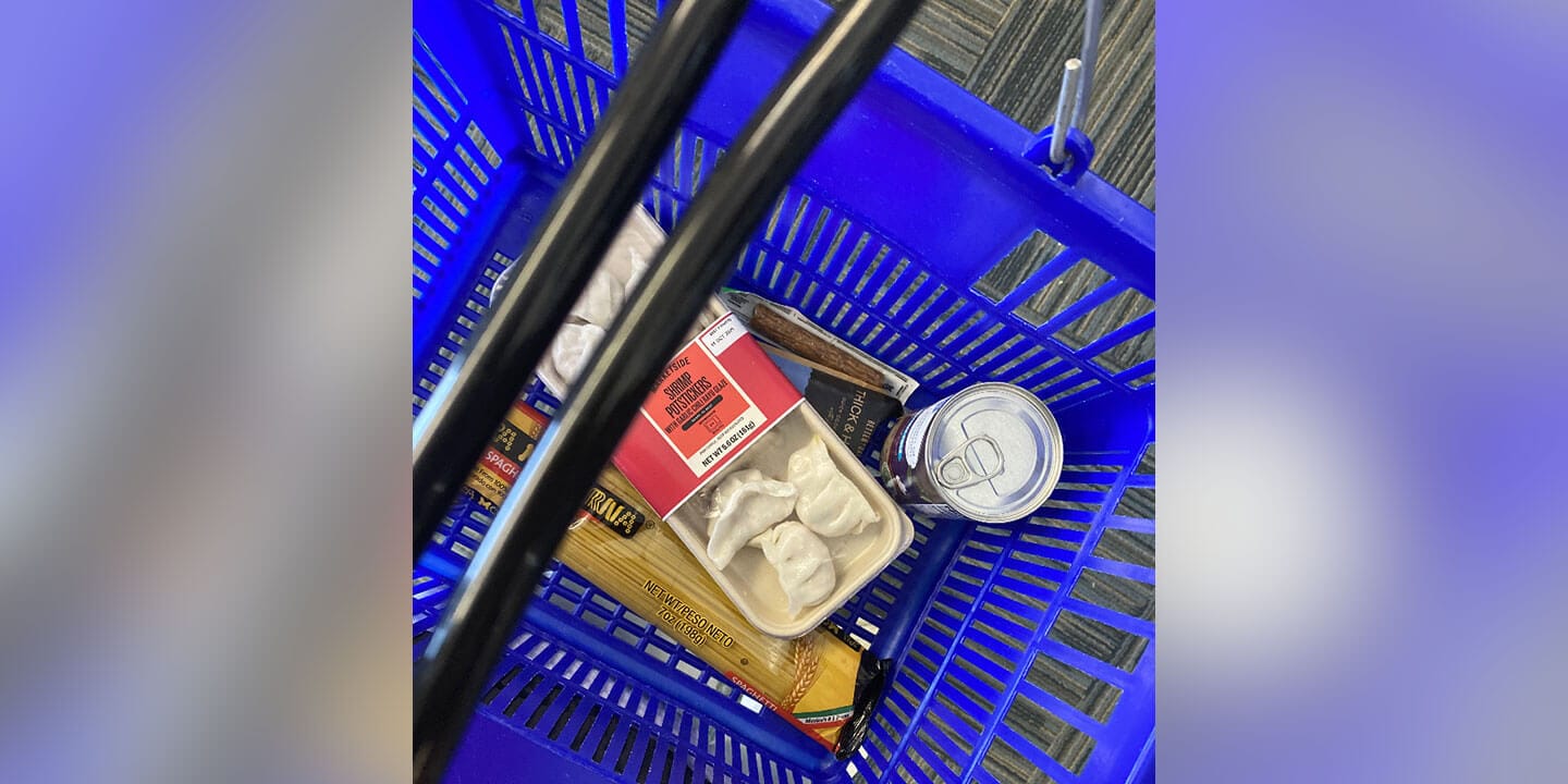 A blue grocery basket filled with various food items including noodles and potstickers.