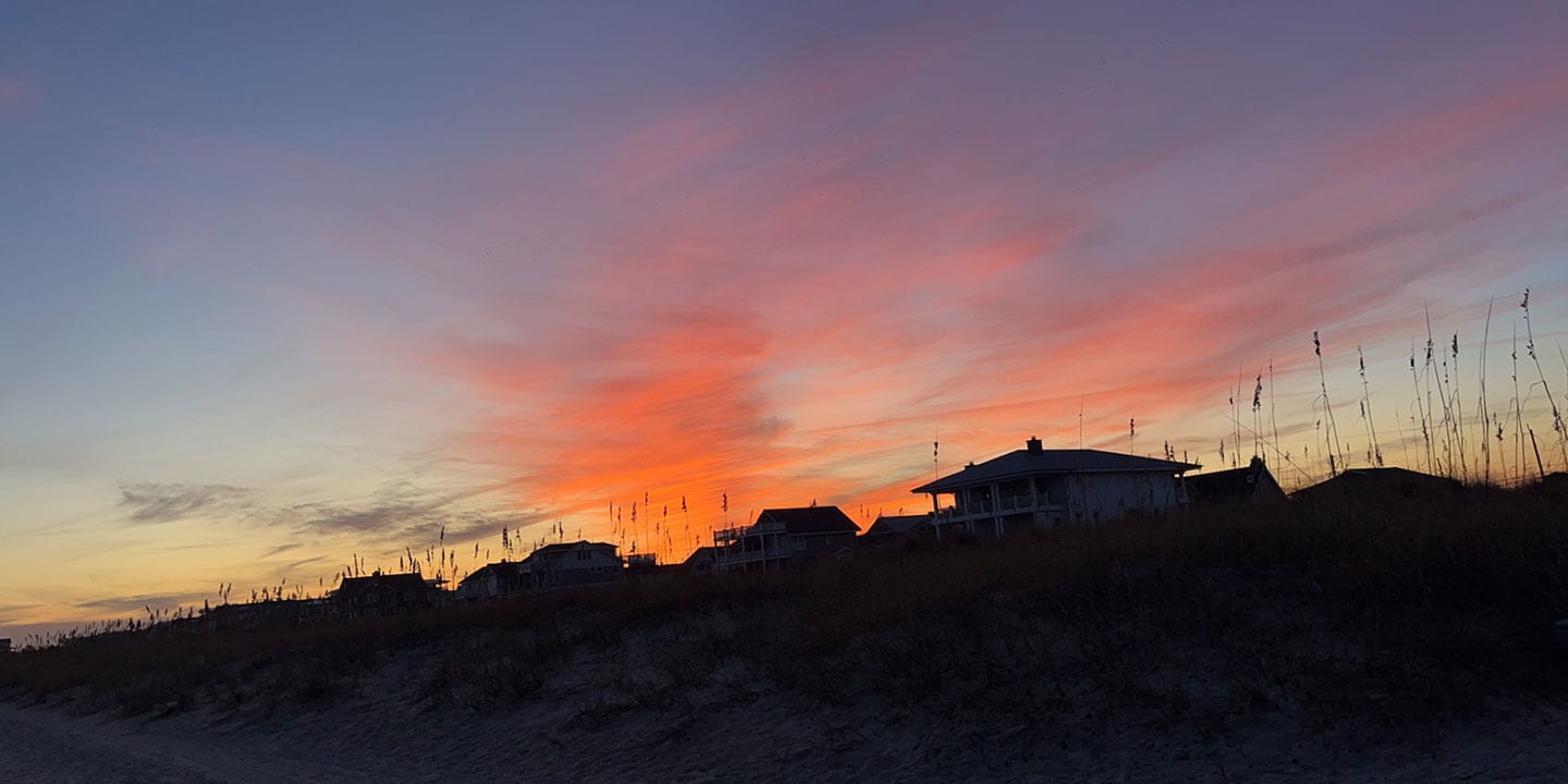 A peaceful scene of beach houses at sunset with tall grasses in the foreground.
