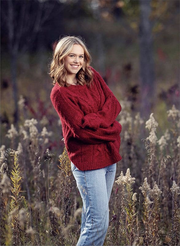 The blog author is standing in a field, has blond hair, and is wearing a red sweater and jeans.