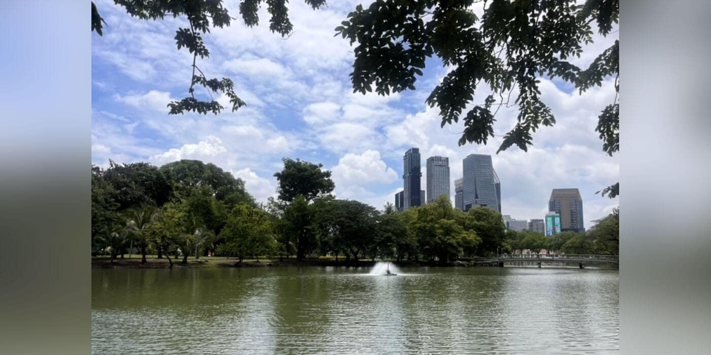 A pond with a fountain in the center and a cityscape in the background.