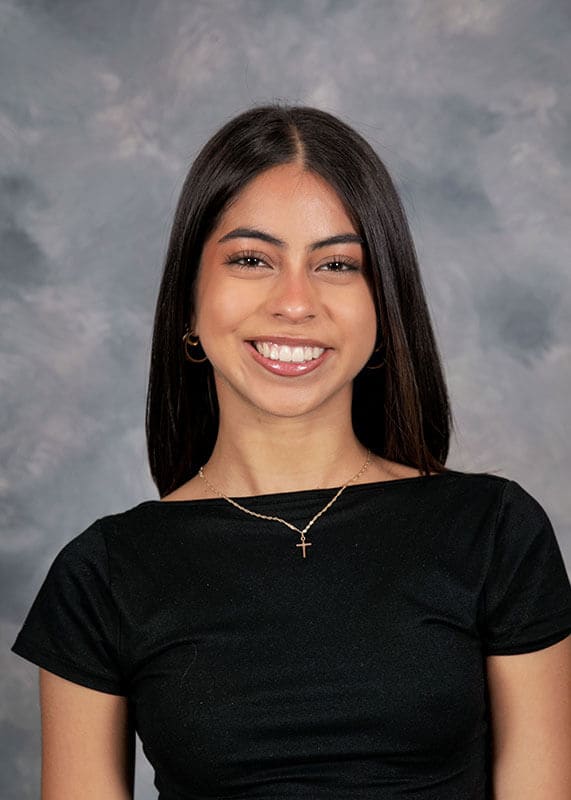 The blog author, Ariana, has long dark hair and is wearing a black shirt with a gold cross necklace.