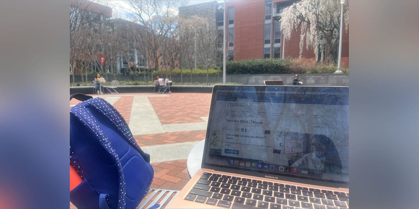 A campus scene showing an open laptop next to a bright blue backpack.