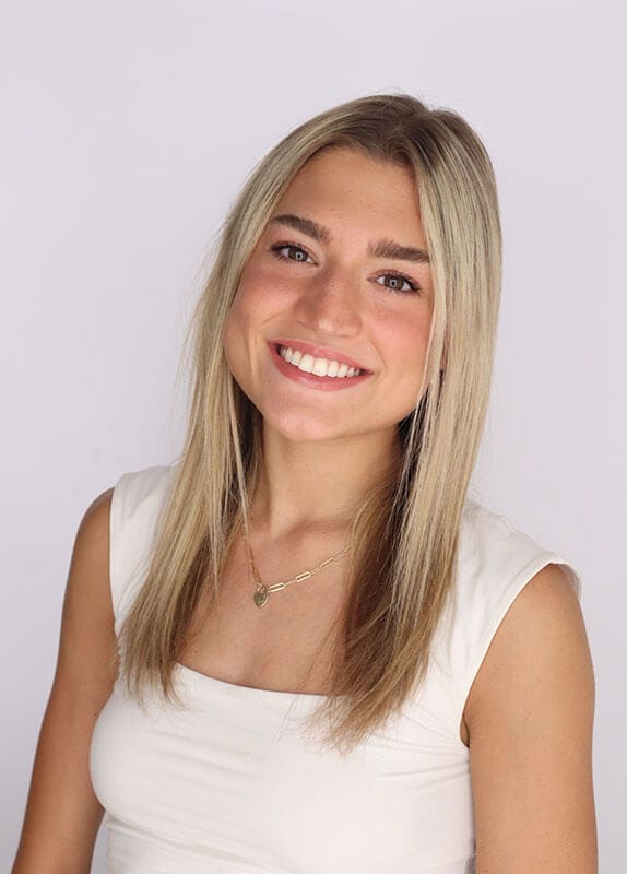 The blog author has long blond hair and is wearing a black off the shoulder top with a gold necklace and gold earrings.