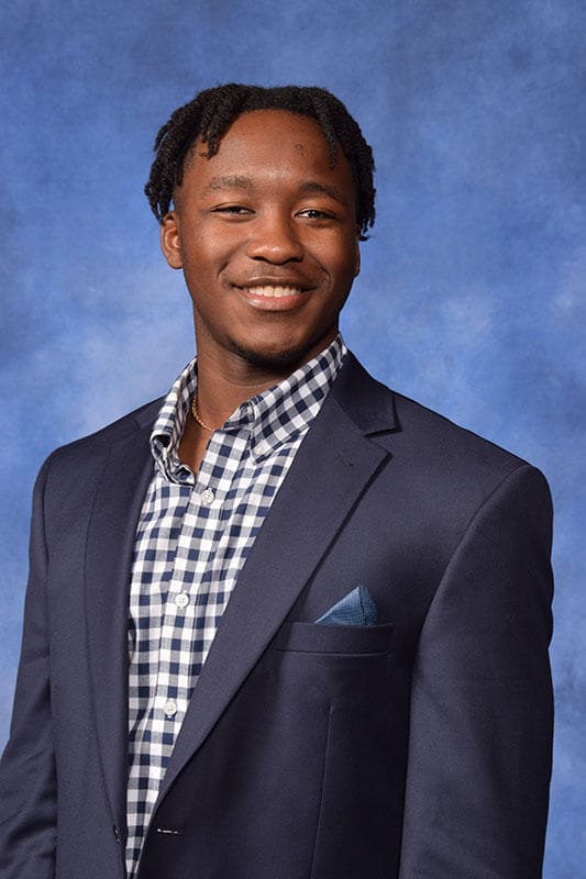 The blog author, Arnold, has dark hair and is wearing a navy blue blazer with a light blue pocket square and a navy and white checkered dress shirt.